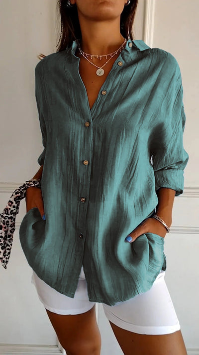 Chemise en lin vert émeraude pour femme, manches longues, boutons en bois, poches avant, portée avec un pantalon blanc. Mode élégante et décontractée.