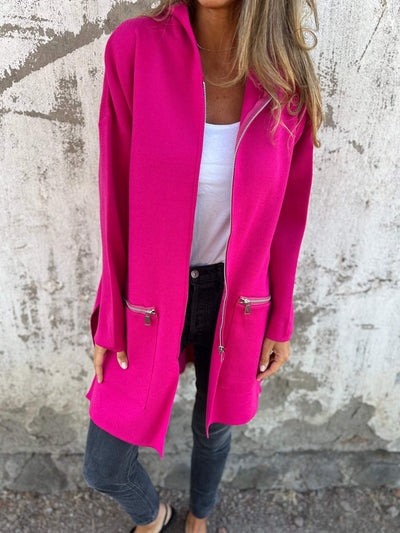 Femme portant un manteau rose vif avec fermetures éclair, sur un mur texturé. Mode automne, style décontracté, tendance féminine.