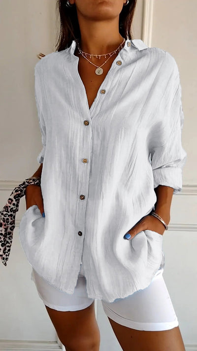 Femme portant une chemise blanche en lin avec boutons en bois, manches retroussées, col ouvert, associée à un pantalon blanc. Mode décontractée élégante.