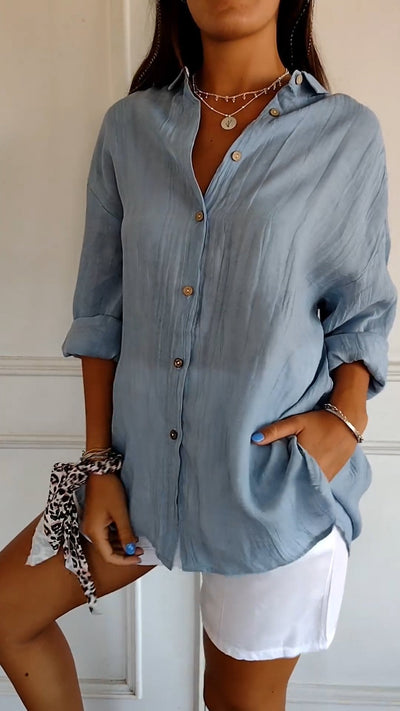 Femme portant une chemise bleue en lin avec boutons, manches retroussées, associée à un short blanc. Style décontracté et élégant.