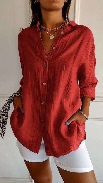 Chemise rouge en lin pour femme, manches longues, boutons en bois, col ouvert, poches avant, portée avec un pantalon blanc. Mode élégante et décontractée.