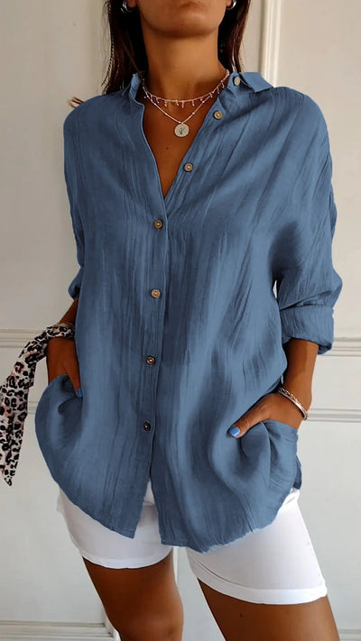 Chemise bleue en lin pour femme avec boutons en bois, manches retroussées, associée à un pantalon blanc. Style décontracté et élégant.