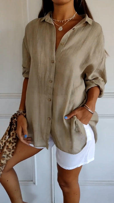 Femme portant une chemise beige ample en lin, manches retroussées, avec short blanc. Accessoires: collier, bracelet, sac imprimé léopard.