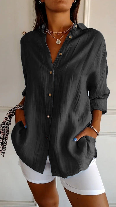 Femme portant une chemise noire ample à manches longues, boutons en bois, avec un pantalon blanc. Style décontracté chic, mode féminine tendance.