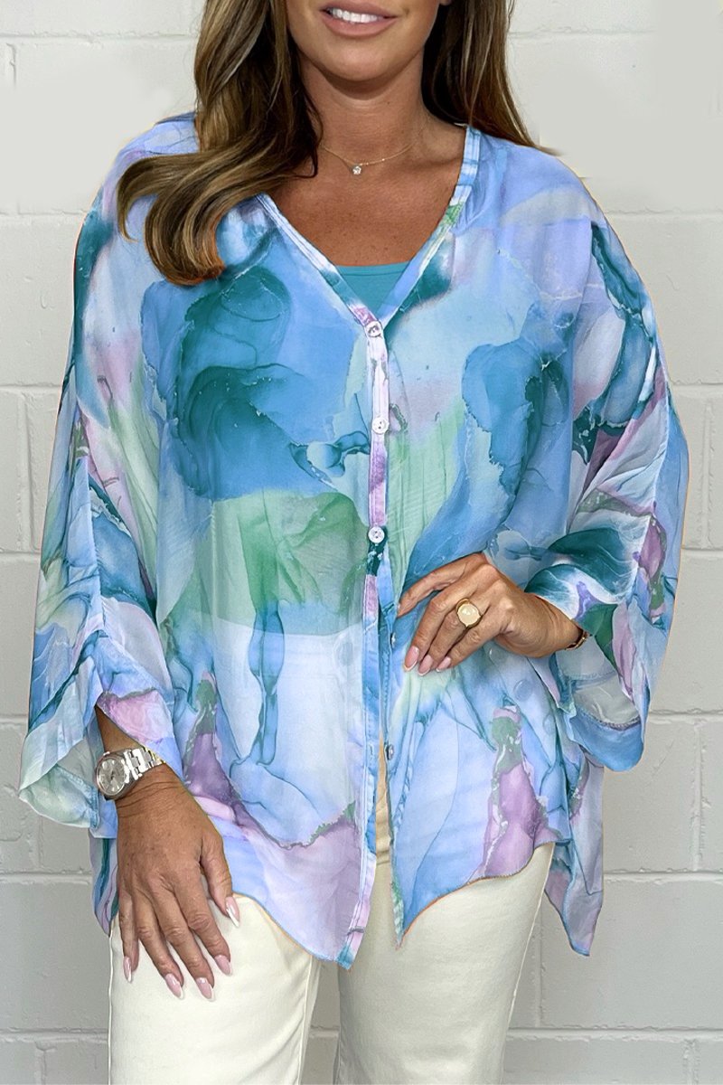 Femme portant une tunique fluide à motifs aquarelle bleu et vert, manches longues, sur fond blanc. Mode féminine élégante et colorée.