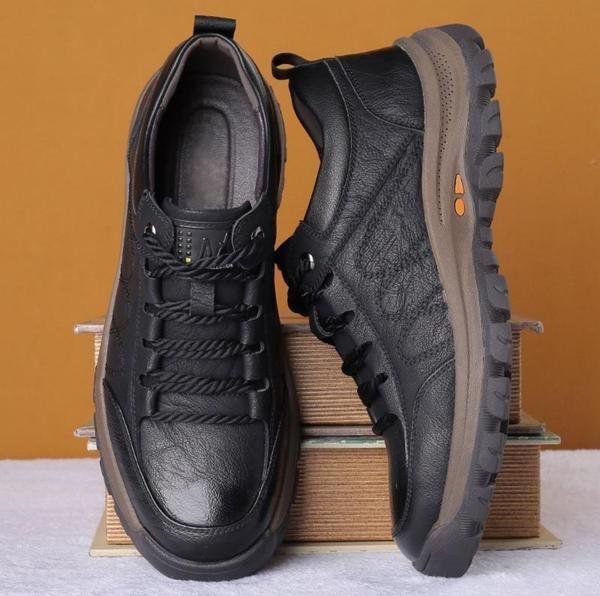 Chaussures de randonnée en cuir noir pour hommes, semelle antidérapante, design robuste, posées sur des livres, fond orange.