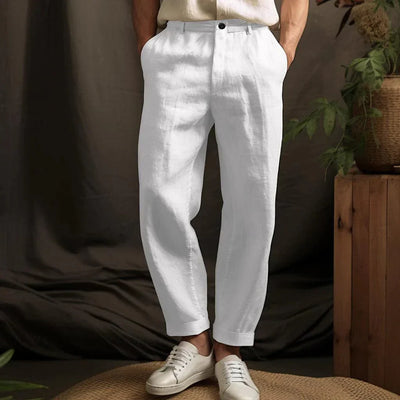 Pantalon blanc en lin pour homme, style décontracté, avec poches, associé à des baskets blanches, ambiance naturelle et élégante.