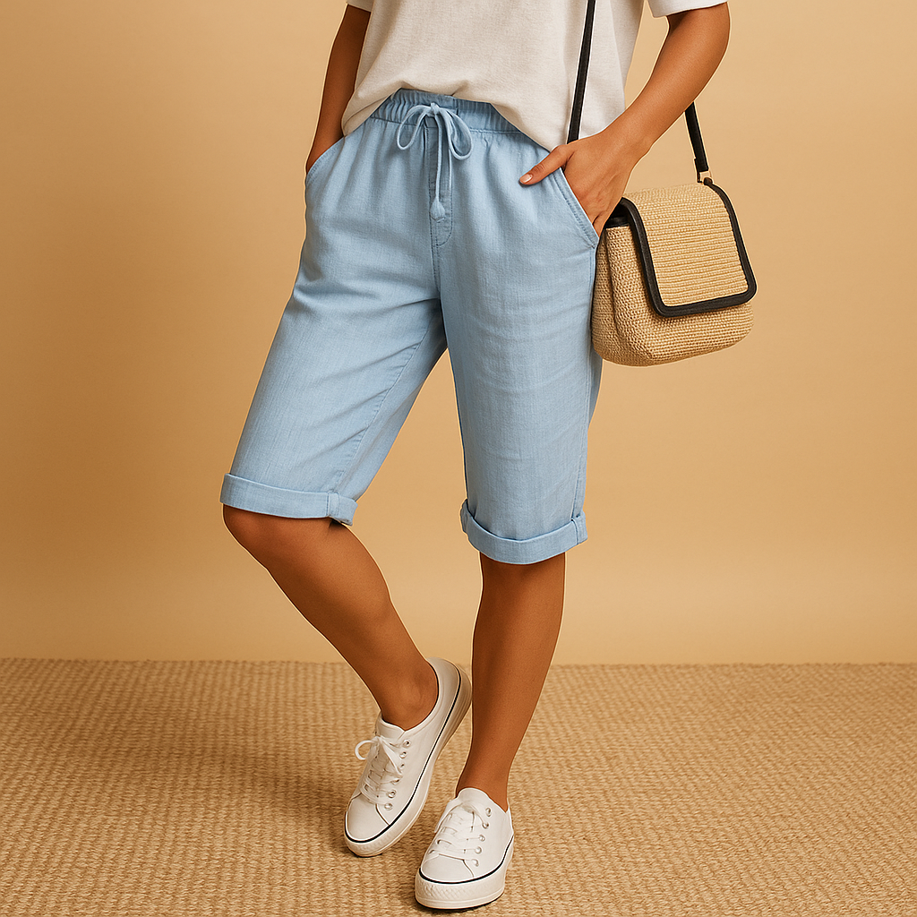Femme portant un short bleu clair, t-shirt blanc et baskets blanches, tenant un sac à main en paille. Mode décontractée, style estival.