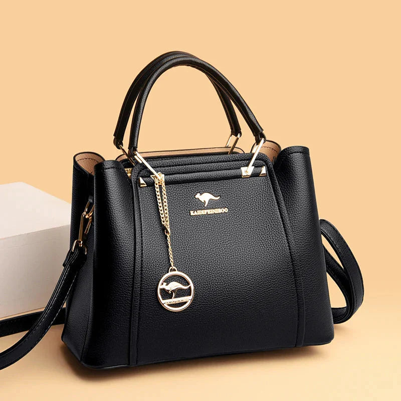 Sac à main noir élégant en cuir avec breloque dorée, design moderne, poignées robustes, fond beige. Accessoire mode femme chic et tendance.