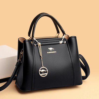 Sac à main noir élégant en cuir avec breloque dorée, design moderne, poignées robustes, fond beige. Accessoire mode femme chic et tendance.