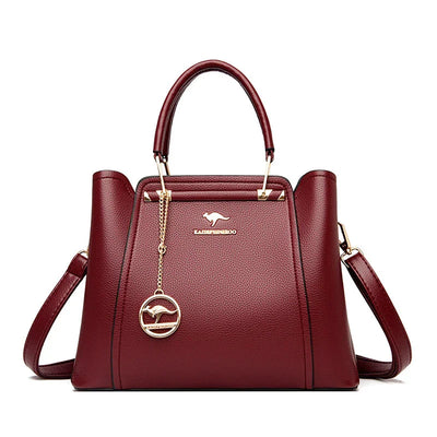 Sac à main en cuir rouge bordeaux élégant avec bandoulière, logo doré et pendentif. Accessoire mode femme chic et tendance.
