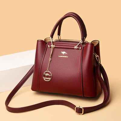 Sac à main en cuir bordeaux élégant avec bandoulière, détails dorés et pendentif logo. Accessoire mode femme chic et tendance.