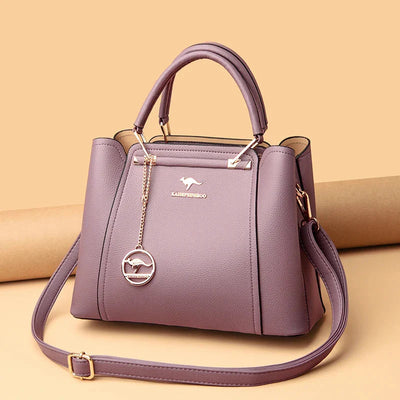 Sac à main en cuir violet élégant avec bandoulière amovible, logo doré et pendentif, sur fond beige. Accessoire mode femme tendance.