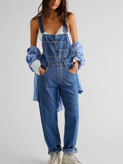 Femme portant une salopette en jean bleu avec une chemise bleue et des baskets blanches, mode décontractée, style urbain tendance.