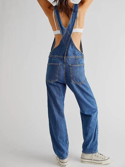 Salopette en jean bleu avec bretelles croisées, portée par une femme de dos, associée à des baskets blanches. Mode décontractée et tendance.