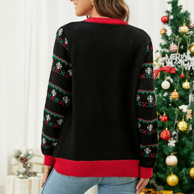 Femme portant un pull de Noël noir avec motifs flocons de neige, manches décorées, devant un sapin de Noël décoré. Mode festive hiver.