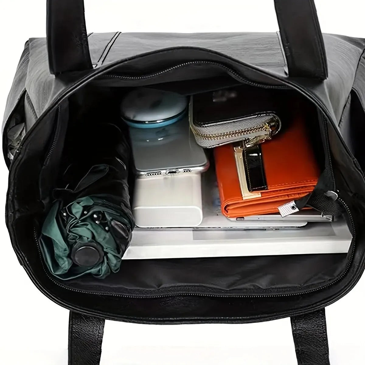 Sac à main noir ouvert avec parapluie, portefeuille, carnet orange, boîte bleue et smartphone à l'intérieur. Accessoires de mode et organisation.