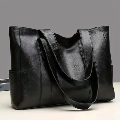 Sac à main en cuir noir élégant avec anses longues, posé sur une surface blanche. Accessoire mode femme, design moderne et spacieux.
