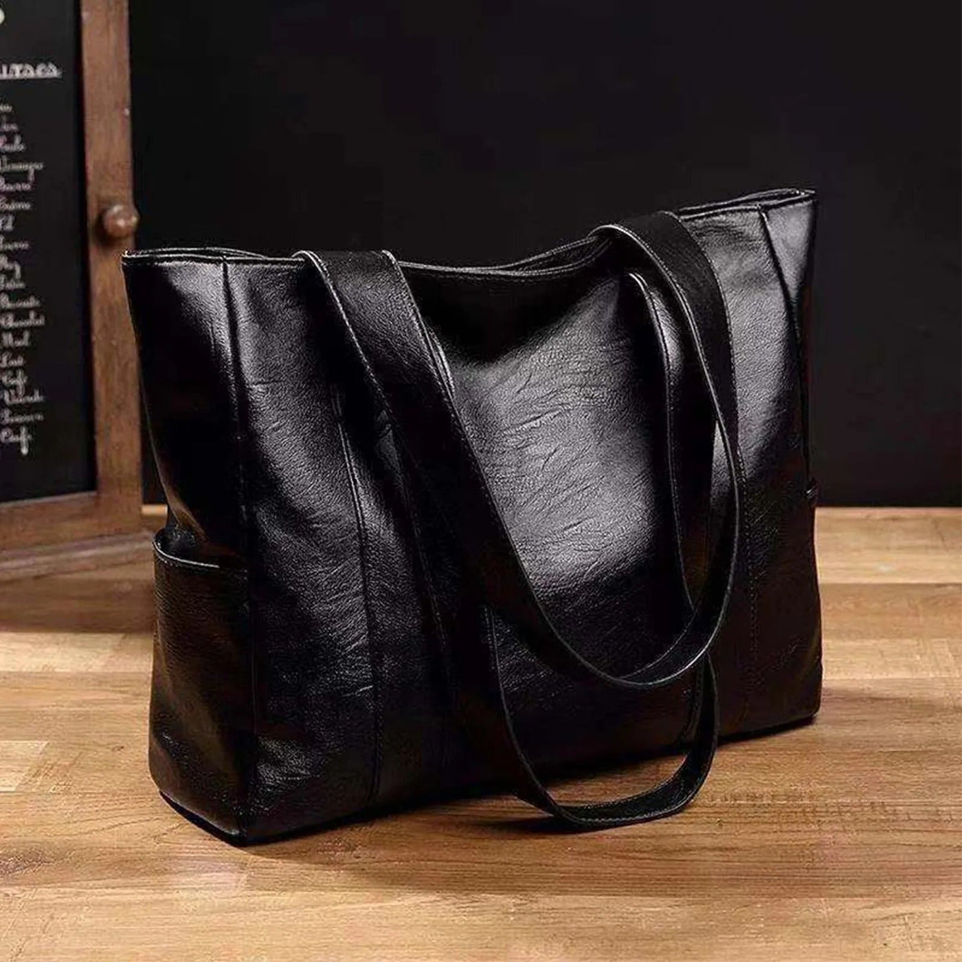 Sac à main en cuir noir élégant sur table en bois, design moderne avec anses longues, parfait pour mode féminine et accessoires tendance.
