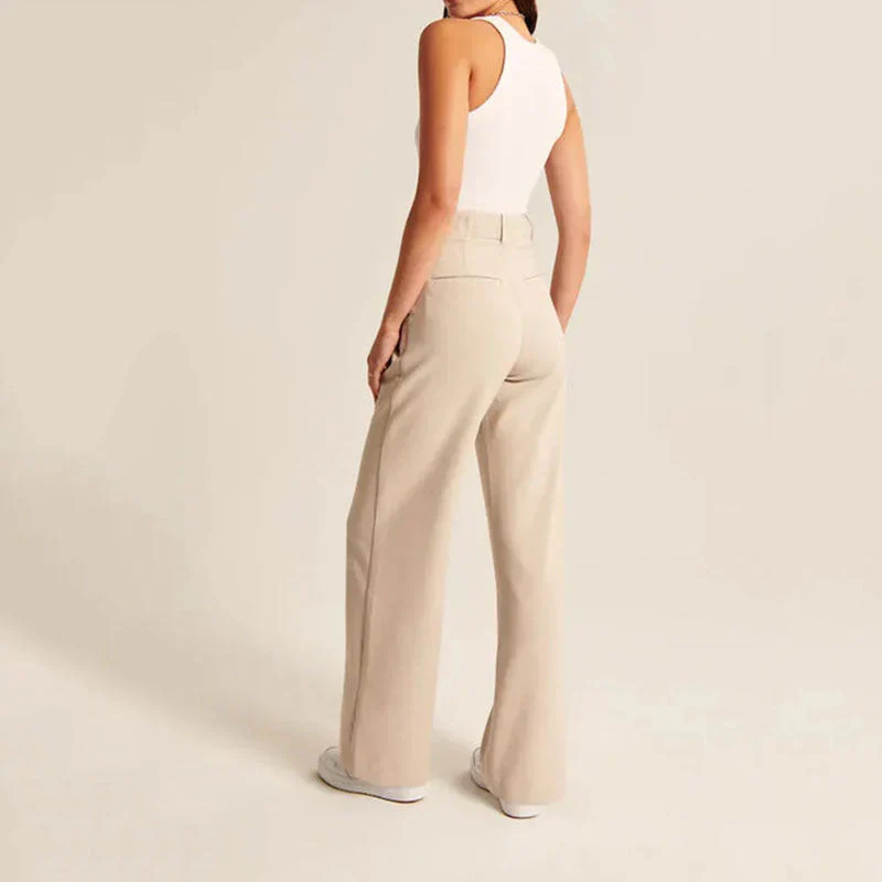 Femme en débardeur blanc et pantalon beige ample, vue de dos, posant dans un studio minimaliste. Mode féminine, tenue décontractée, style moderne.