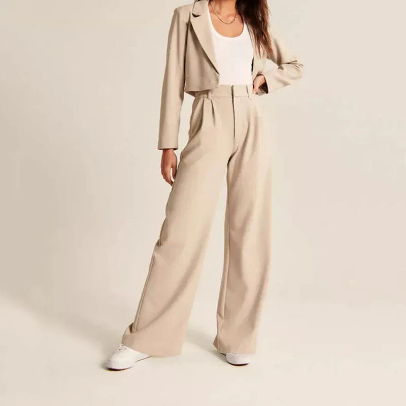 Femme en tailleur beige élégant, veste courte et pantalon large, portant un débardeur blanc et des baskets blanches. Mode chic et décontractée.