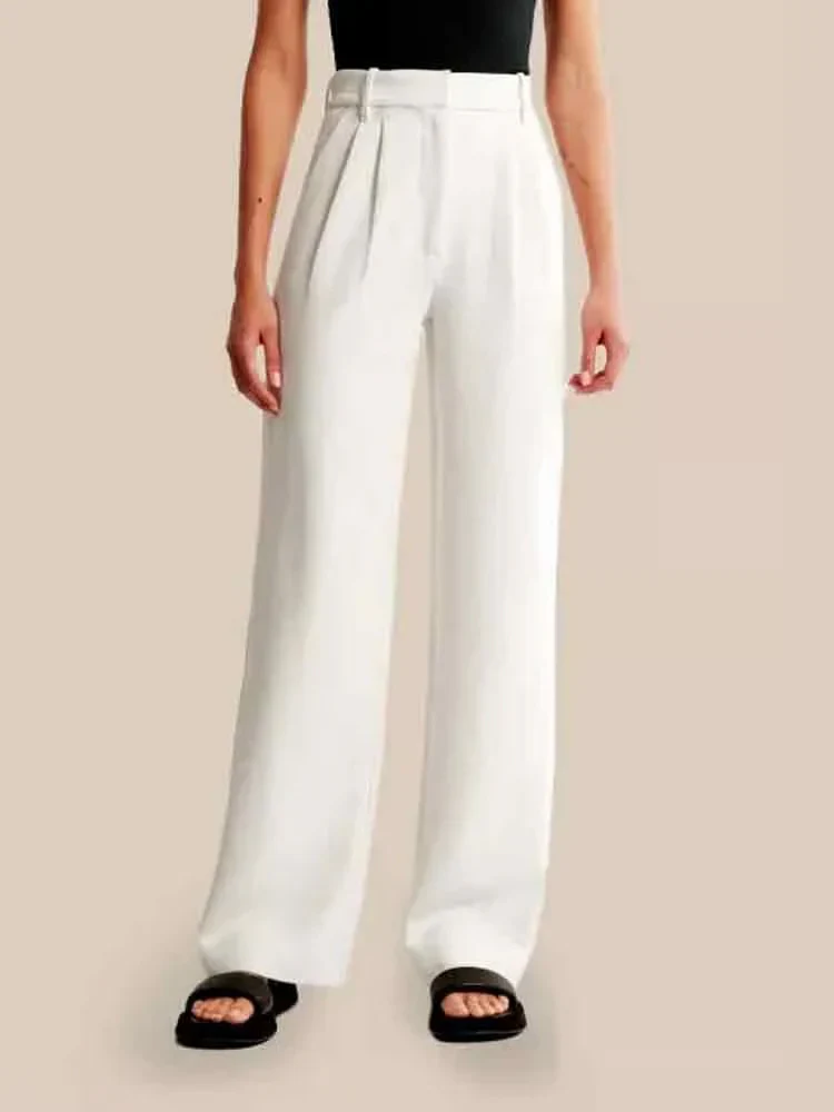 Pantalon large blanc pour femme, taille haute, avec pinces, porté avec un haut noir sans manches et des sandales noires. Mode élégante et moderne.