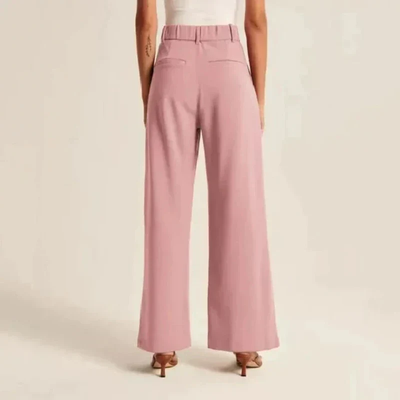 Pantalon large rose femme, taille haute, poches arrière, porté avec un haut blanc. Mode élégante, tendance, style décontracté chic.