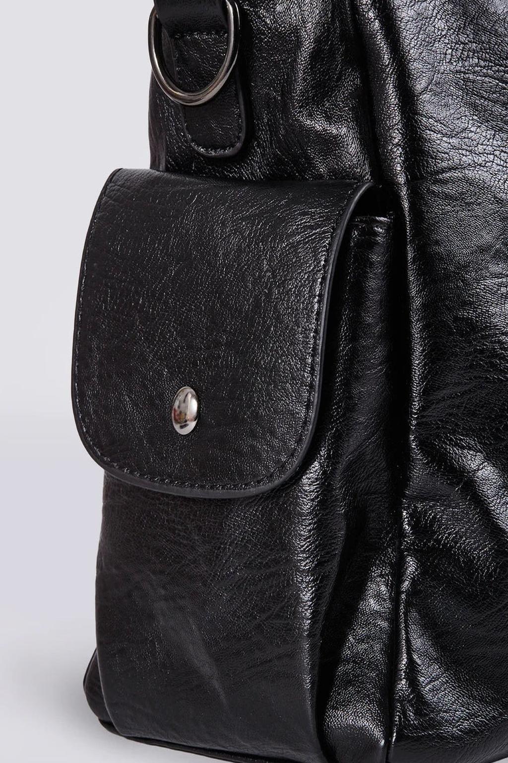 Sac à dos en cuir noir texturé avec poche avant à bouton-pression, anneau métallique et coutures visibles. Accessoire mode élégant et pratique.