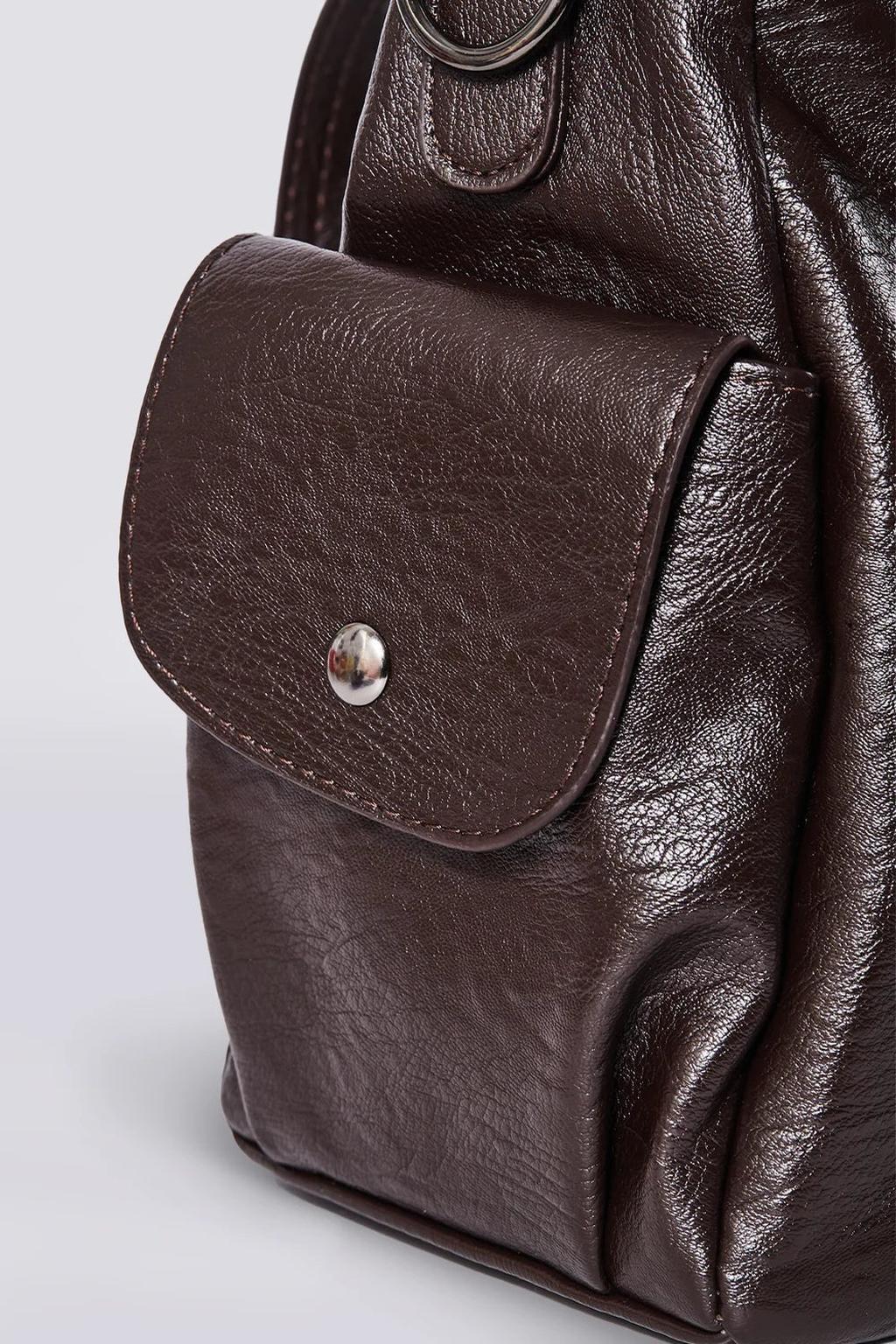 Sac à dos en cuir marron foncé avec poche avant à bouton-pression, texture grainée, design élégant et moderne. Accessoire mode tendance.