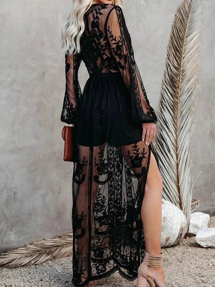 Robe longue noire en dentelle transparente avec motifs floraux, manches longues, fendue, portée par une femme blonde, style élégant et chic.