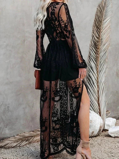 Robe longue noire en dentelle transparente avec motifs floraux, manches longues, fendue, portée par une femme blonde, style élégant et chic.