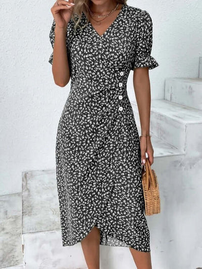 Robe à fleurs noires et blanches avec manches courtes et boutons, portée par une femme tenant un sac en osier, style estival élégant.