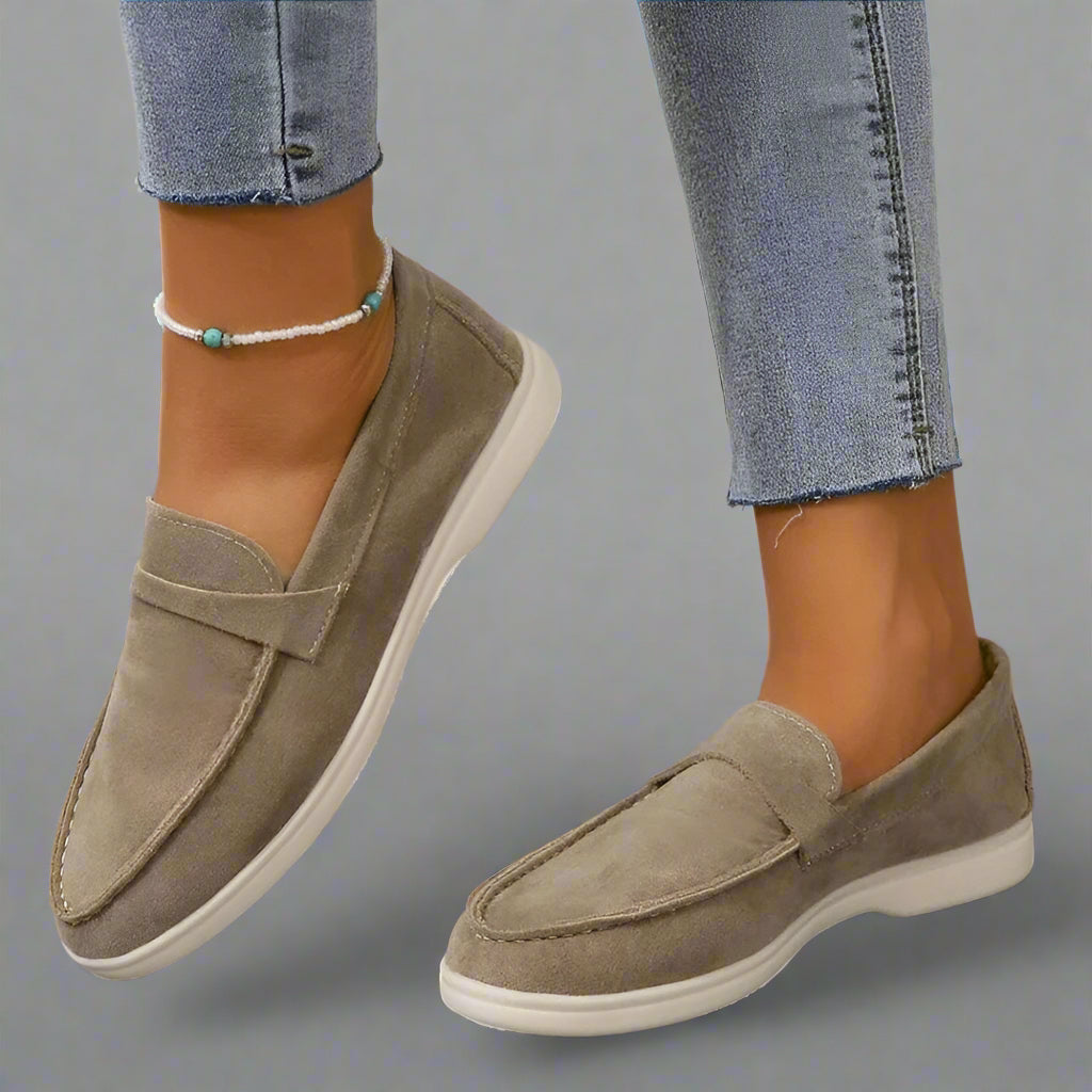 Chaussures mocassins en daim beige pour femme, portées avec un jean ajusté. Style décontracté, confort et élégance. Accessoire cheville perlé.