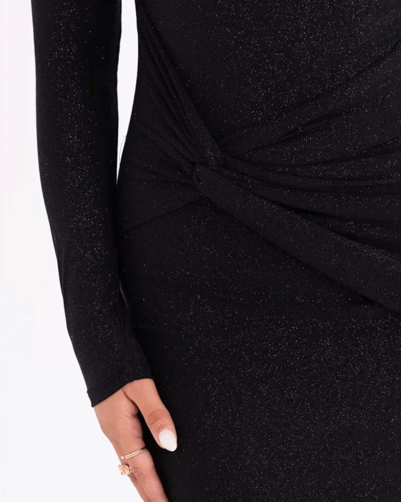 Robe noire scintillante à manches longues, détail drapé à la taille, main avec bague dorée. Mode élégante, tenue de soirée chic.