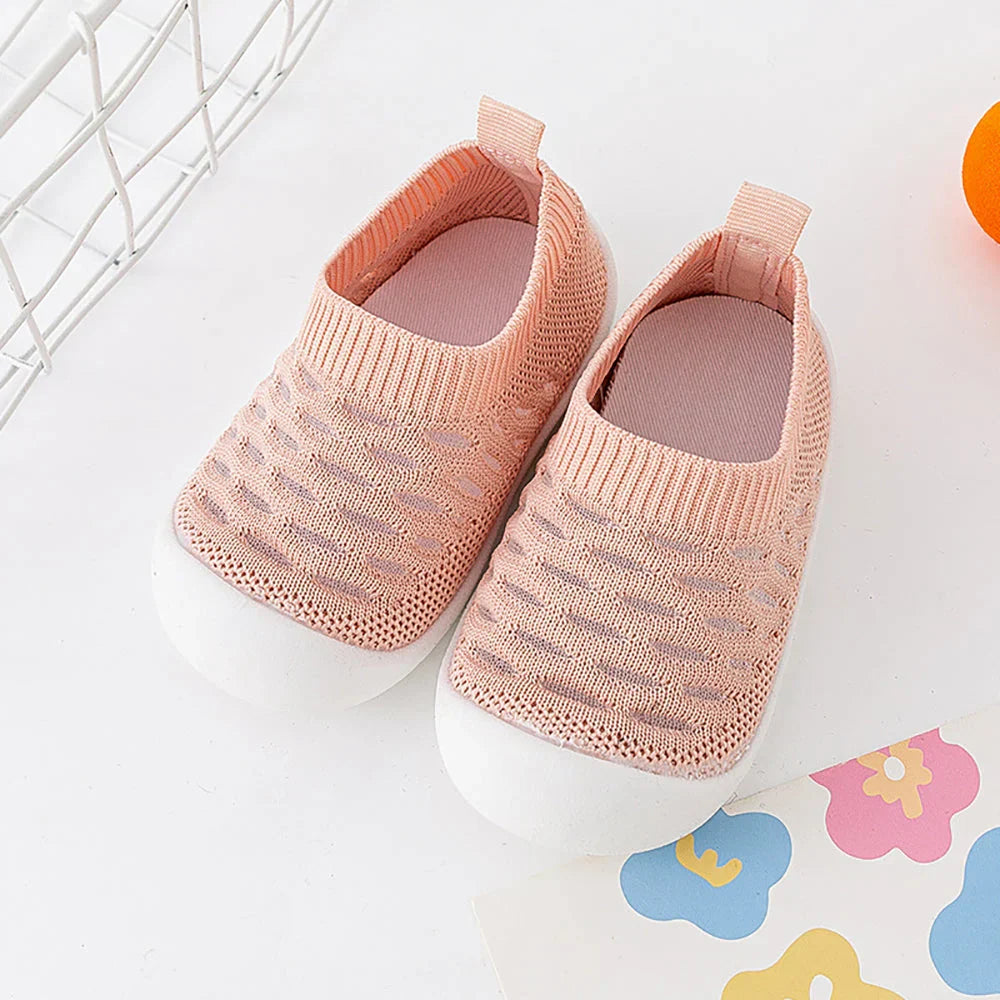 Chaussures bébé roses en maille respirante avec semelle blanche, posées sur fond blanc. Design confortable et moderne pour enfants.