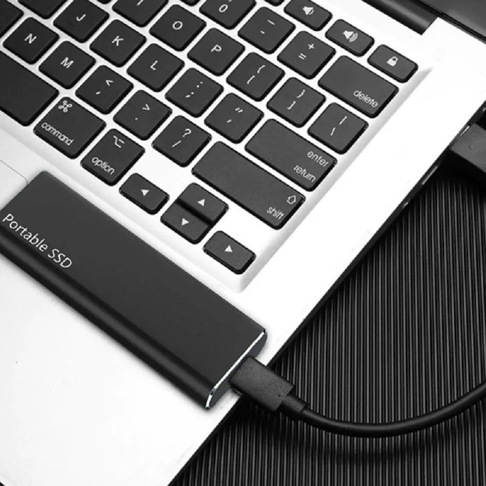 Disque SSD portable connecté à un ordinateur portable via un câble USB, posé sur un clavier argenté. Stockage externe rapide et compact.