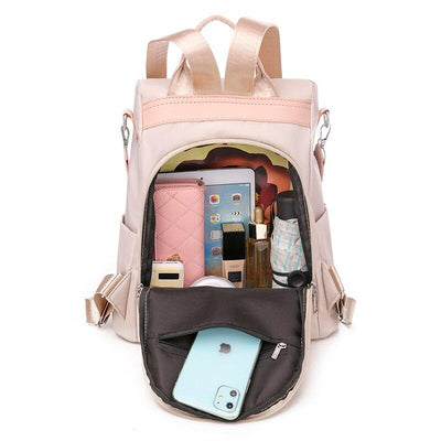 Sac à dos beige ouvert avec compartiments organisés, contenant un iPhone, portefeuille rose, tablette, bouteilles et accessoires. Idéal pour voyage.