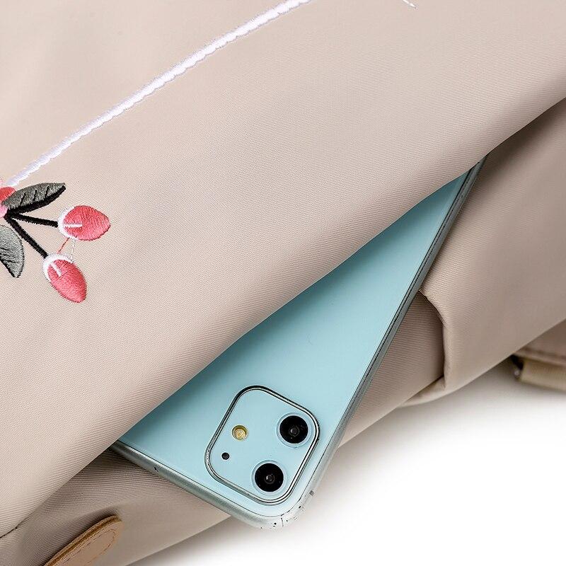 Sac beige avec broderie florale, contenant un smartphone bleu à double caméra. Accessoire mode tendance, idéal pour le quotidien.
