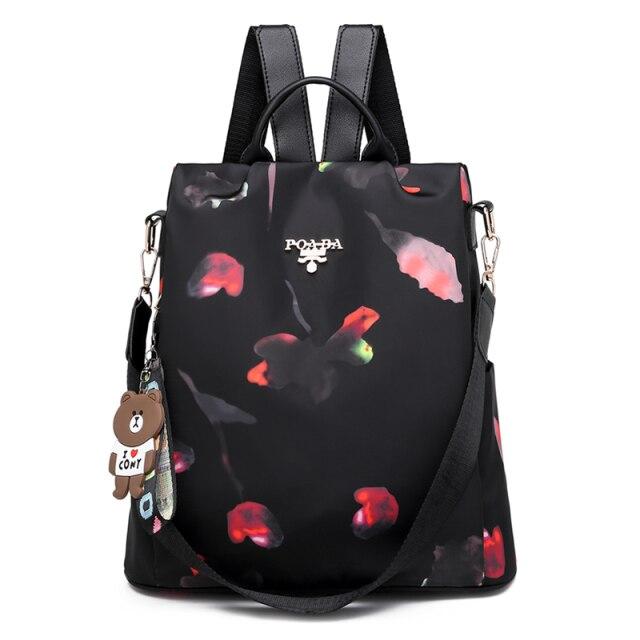 Sac à dos noir élégant avec motif floral abstrait, bretelles ajustables, porte-clés ours en peluche, idéal pour mode féminine et usage quotidien.