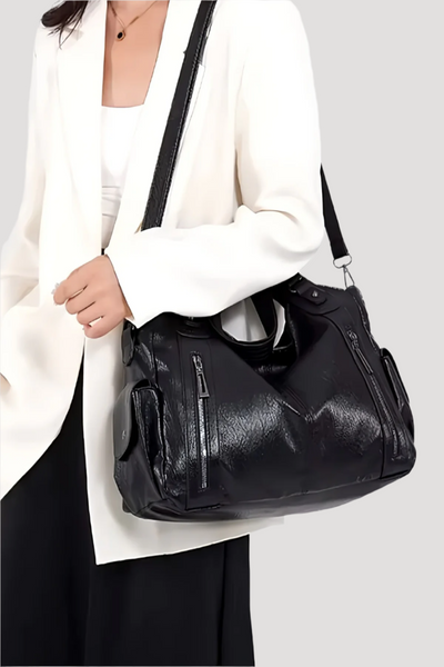 Sac à main noir en cuir porté par une femme en blazer blanc, design élégant avec fermetures éclair, accessoire de mode chic et moderne.