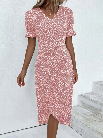 Robe midi fleurie rose à manches bouffantes, col en V, boutonnée, portée par une femme sur fond de mur blanc et escaliers. Mode féminine élégante.