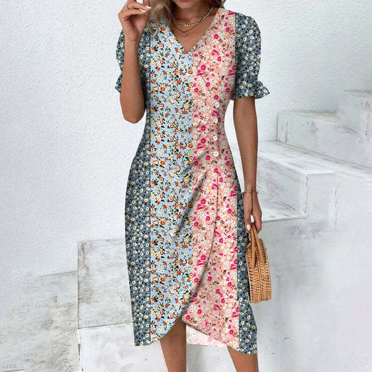 Robe femme à motifs floraux multicolores, manches courtes, col en V, style bohème chic, portée par une femme sur fond d'escalier blanc.