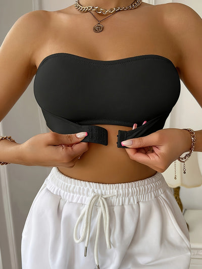 Femme ajustant un haut bandeau noir avec fermeture à crochet, portant un pantalon blanc à taille élastique. Mode estivale, style décontracté.