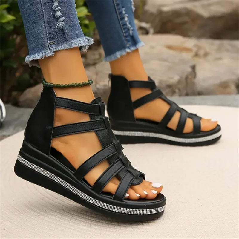 Sandales compensées noires pour femme, design à lanières croisées, portées avec un jean déchiré. Chaussures d'été tendance et confortables.