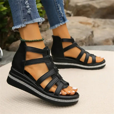 Sandales compensées noires pour femme, design à lanières croisées, portées avec un jean déchiré. Chaussures d'été tendance et confortables.