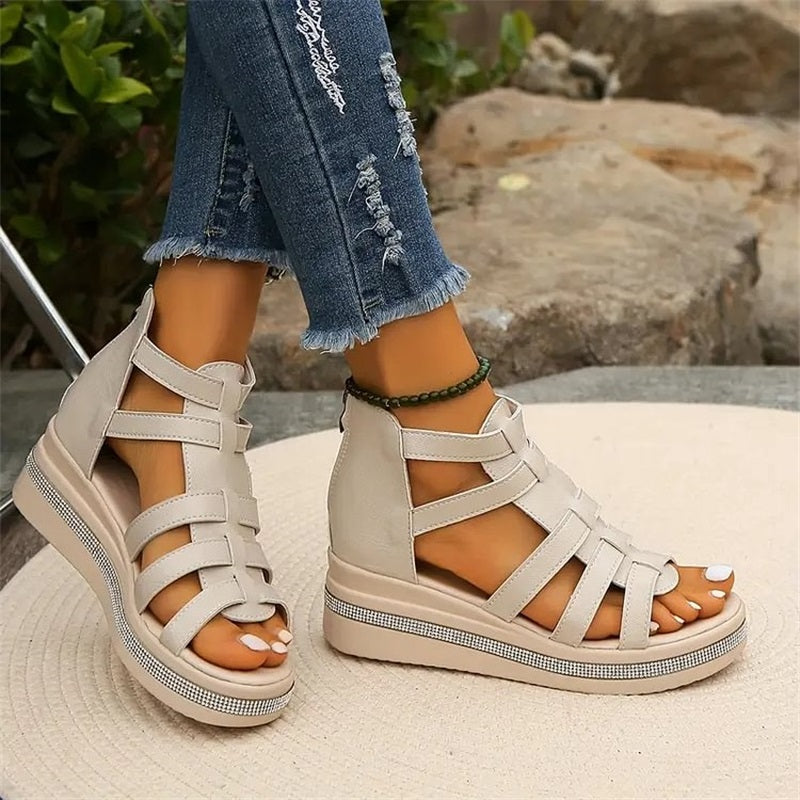 Sandales compensées beiges pour femme, style gladiateur, portées avec un jean déchiré. Chaussures d'été tendance sur fond de jardin.
