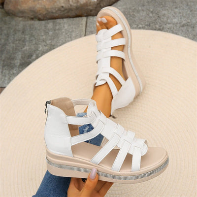Sandales blanches à plateforme avec lanières croisées, semelle épaisse et fermeture éclair arrière, posées sur un tapis beige. Mode estivale femme.
