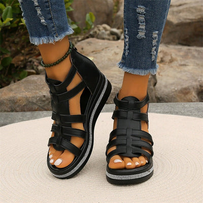 Sandales noires à lanières pour femme, avec semelle plateforme et détails brillants, portées avec un jean déchiré. Mode estivale tendance.