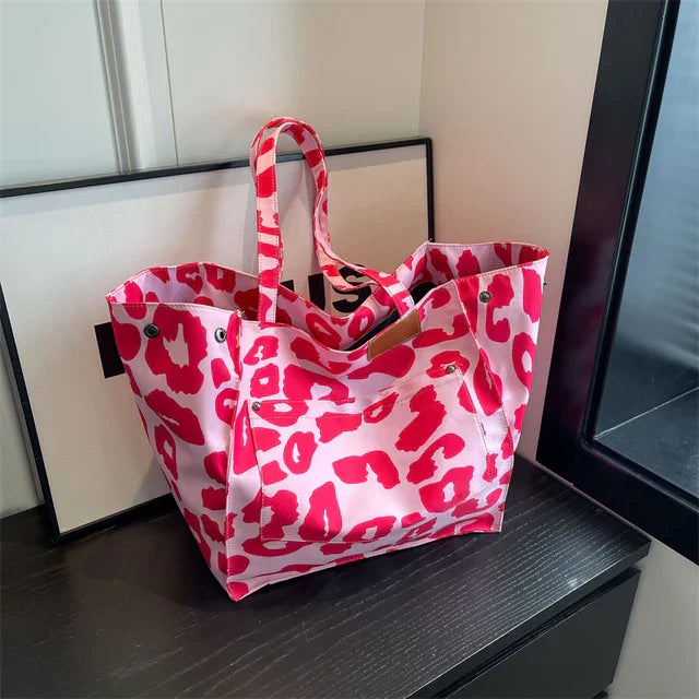 Sac à main rose à motifs léopard rouges, posé sur une table noire près d'une fenêtre. Accessoire de mode tendance, idéal pour un look audacieux.