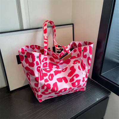 Sac à main rose à motifs léopard rouges, posé sur une table noire près d'une fenêtre. Accessoire de mode tendance, idéal pour un look audacieux.